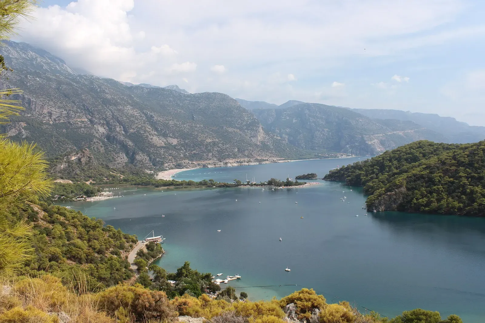 Calm lagoon enclosed by green wooded headlands with steep mountains behind, seen from a pine-covered hillside — Fethiye & Ölüdeniz