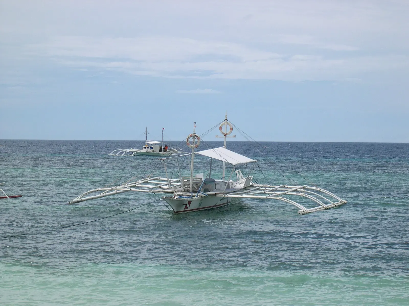 A traditional outrigger bangka anchored over clear water off Panglao
