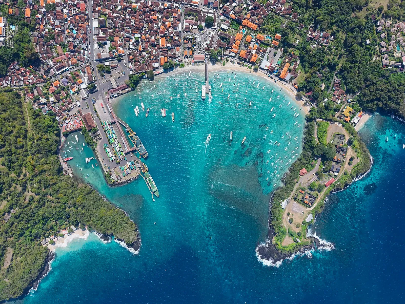 Aerial view of a turquoise bay ringed by a village, a ferry harbour and two green headlands — Padangbai & Candidasa