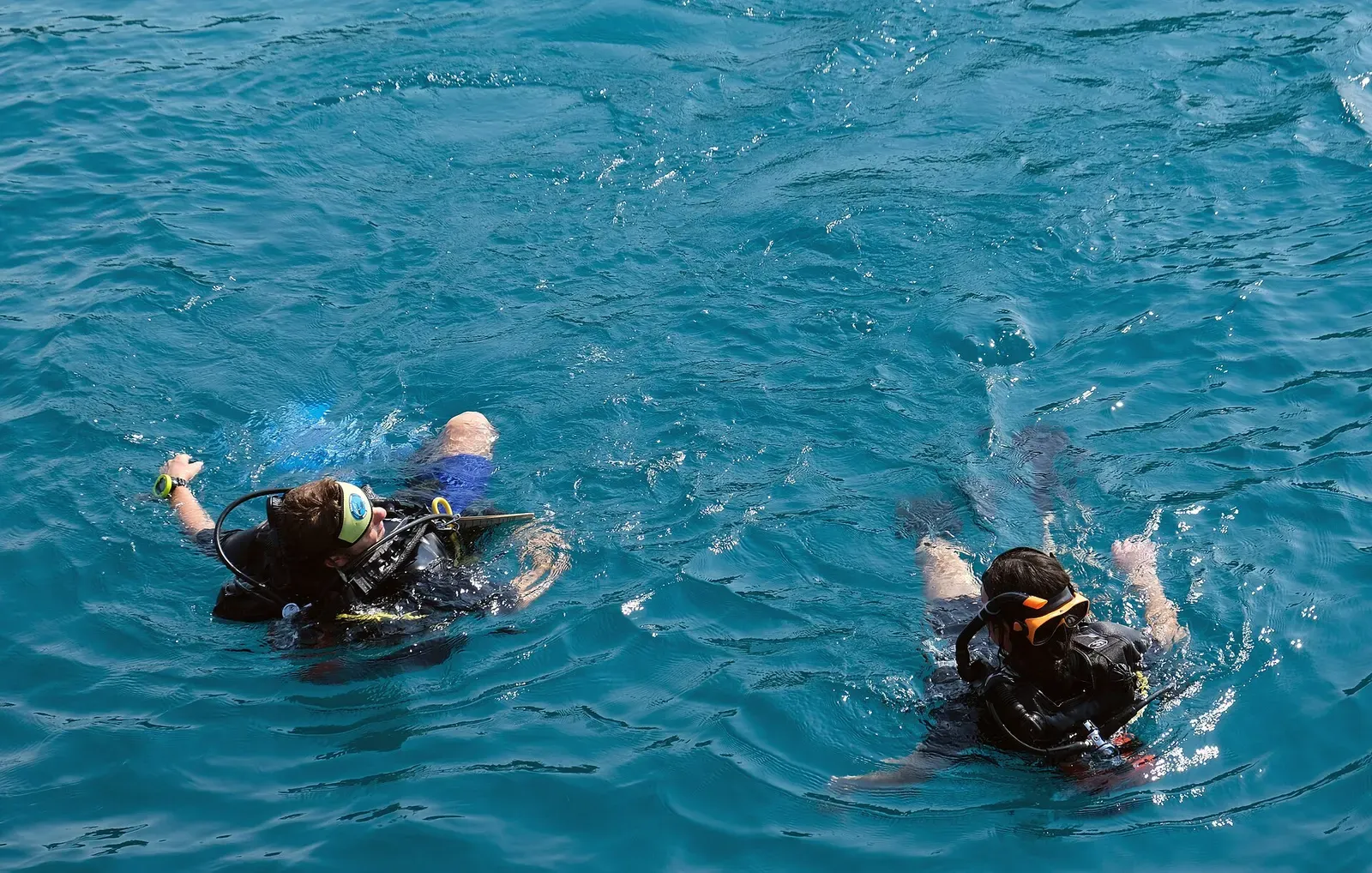 Two scuba divers in black wetsuits and masks float at the surface of blue-green water, seen from above — Ko Ma Ping, Koh Kood & Koh Mak.