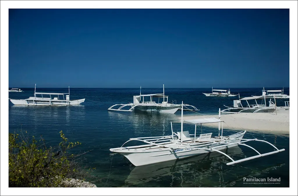 Outrigger boats moored in deep blue water off the shore of Pamilacan Island