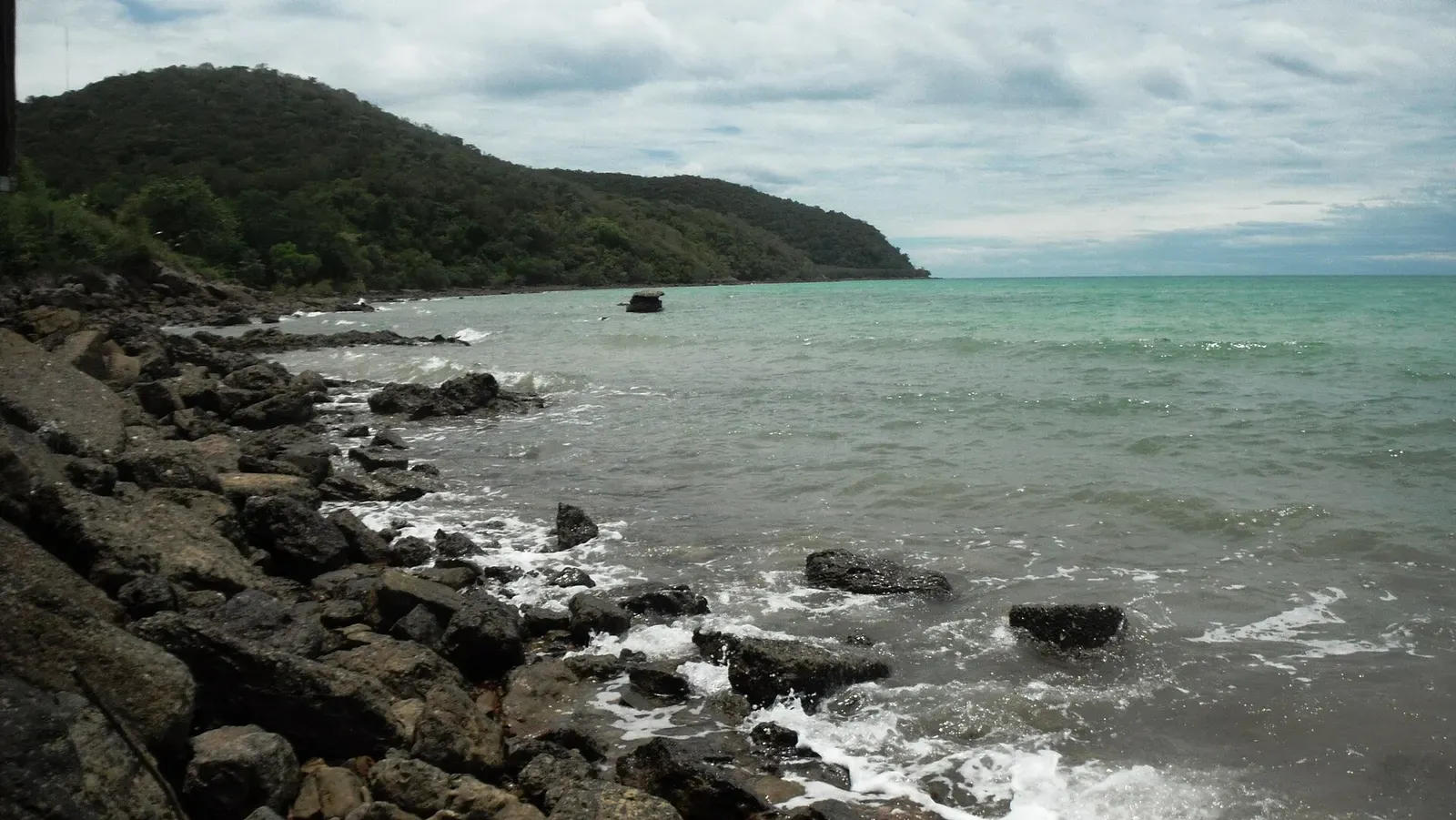 Rocky headland and breaking waves along the Sattahip coastline, with a small boat offshore.