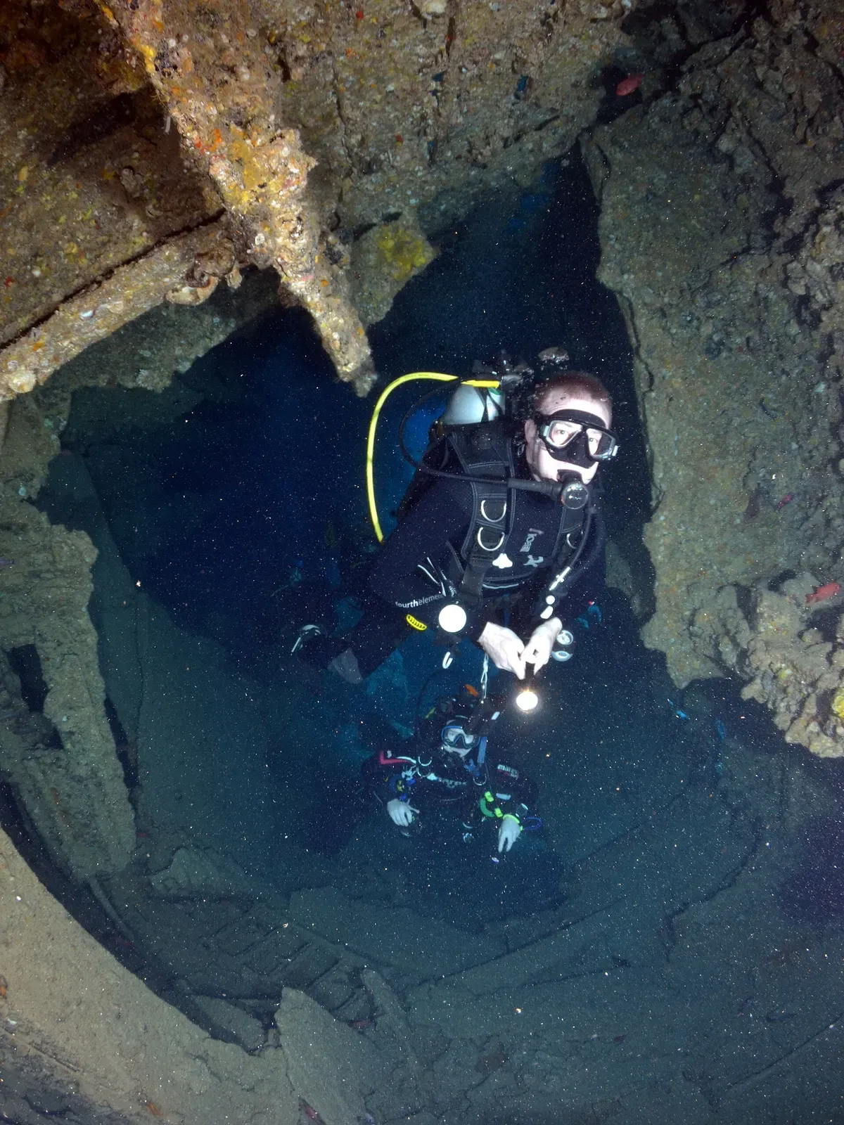 Diver with a torch inside a broken, coral-covered section of the Dunraven's inverted hull — SS Dunraven, Sharm El Sheikh.