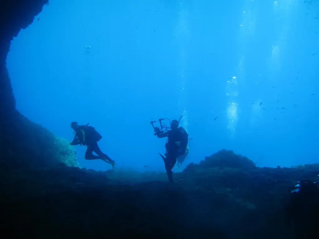 Two divers over rocky reef in clear blue water outside a cavern — Crete