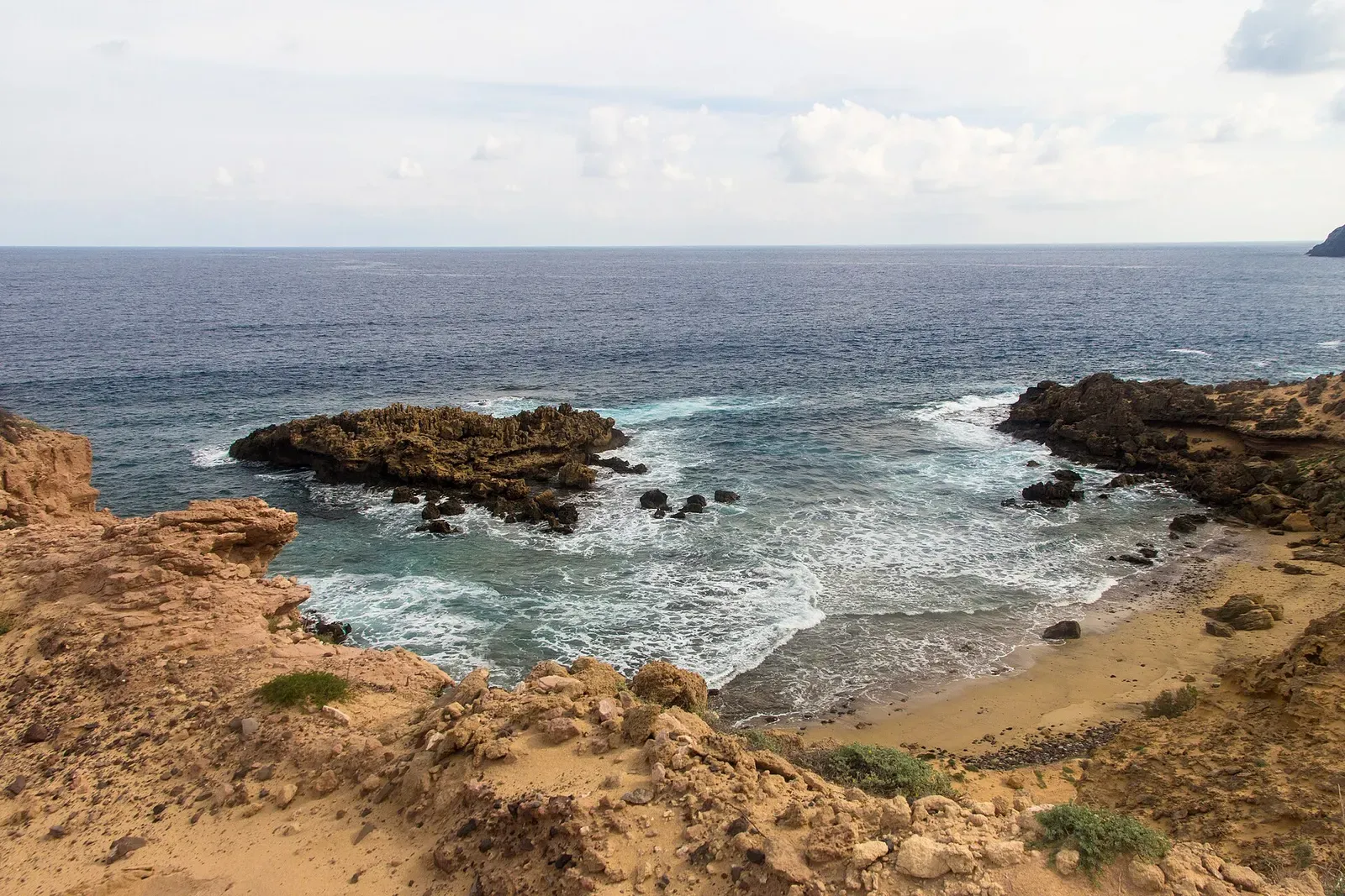 A rocky cove on Porto Santo's coastline with waves breaking on the sand, seen from the cliffs above