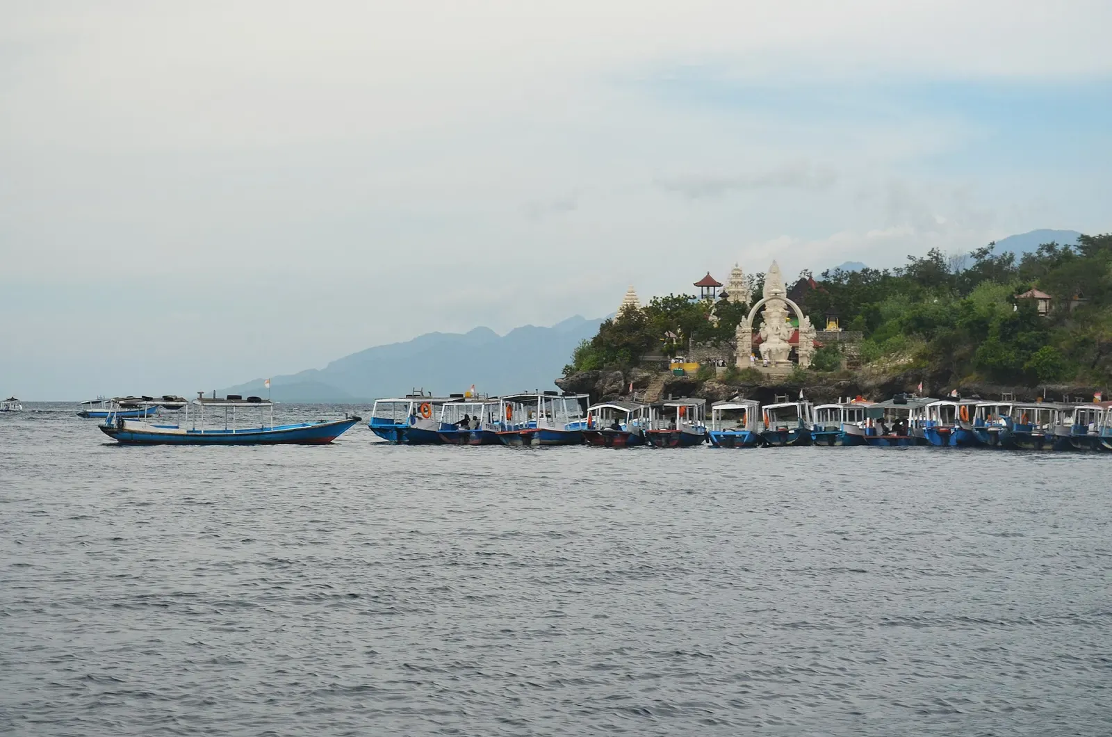 Dive boats anchored off Menjangan Island with the cliffside temple visible among the trees above the shoreline — Temple Wall.