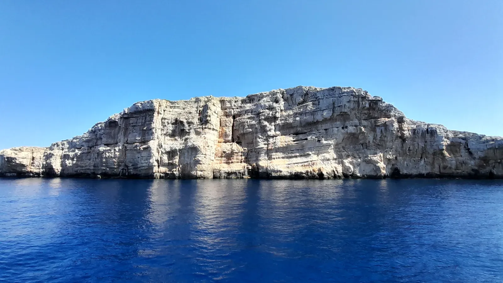 Sunlit limestone cliff face of Rašip Veli dropping into deep blue water in Kornati National Park — Kornati Islands