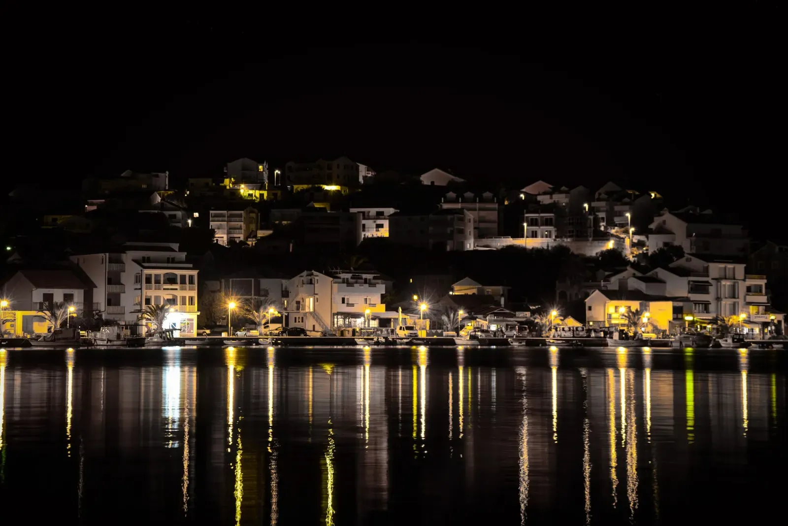 Harbourfront lights reflected on calm water in Rogoznica at night.