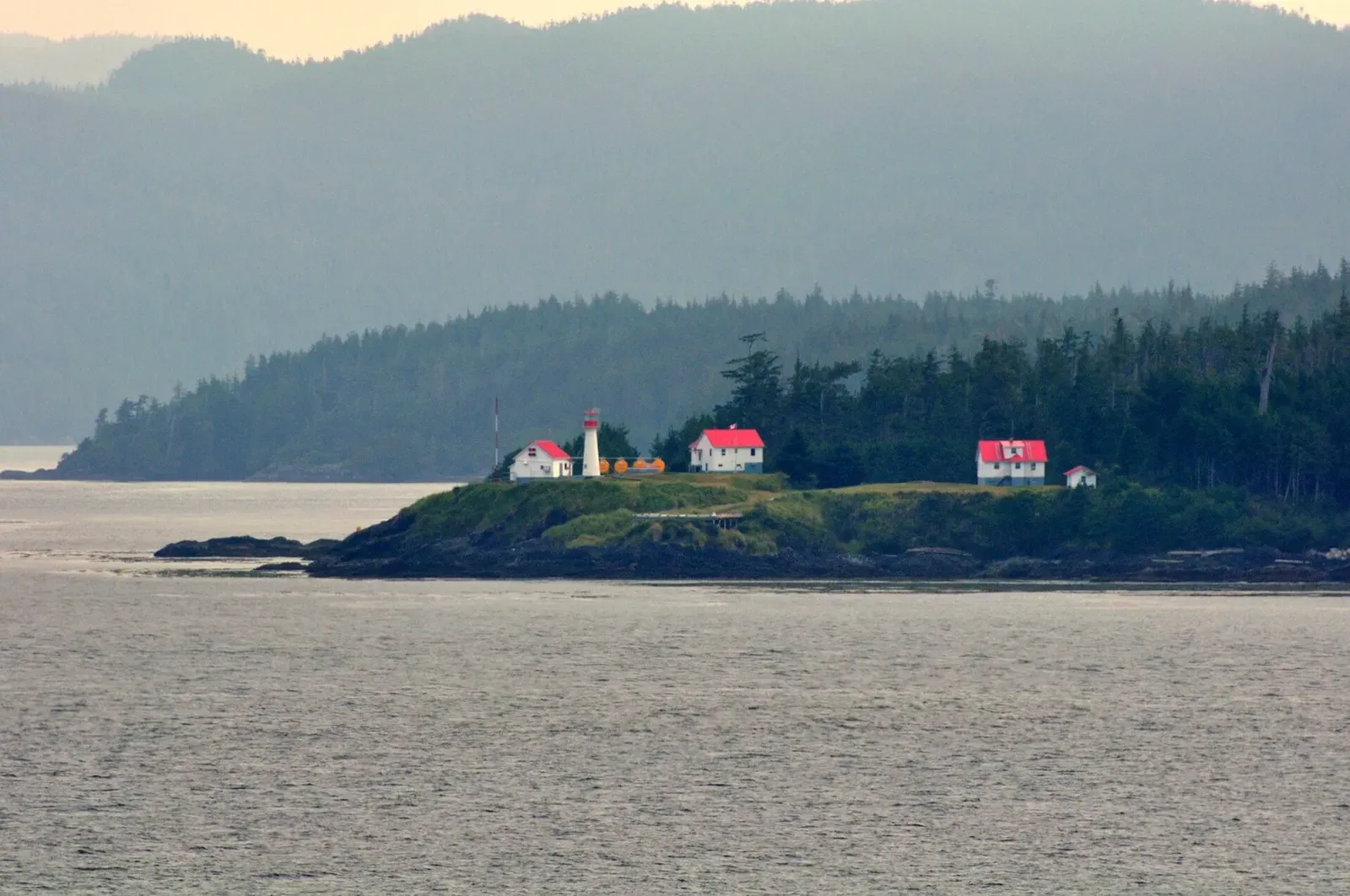 A red-roofed lighthouse station sits on a forested point above the water near Port Hardy — British Columbia