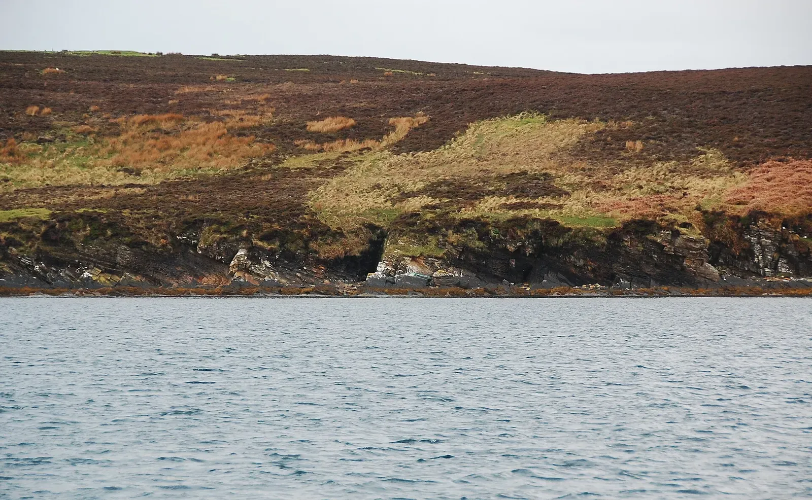 Small sea cave and layered rock ledges along Cava's shoreline at the waterline — SMS Markgraf, Scapa Flow.