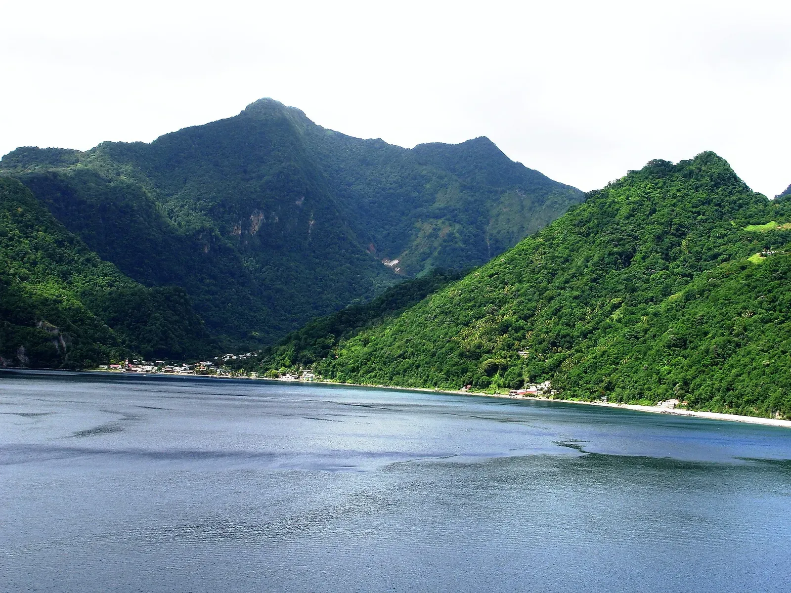 Calm blue water of Soufriere Bay framed by forested mountains rising from the shore — L'Abym, Dominica