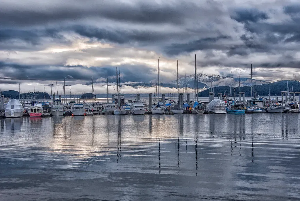 Rows of fishing and pleasure boats moored at Statter Harbor under heavy grey cloud, mirrored in calm water — Juneau & Auke Bay