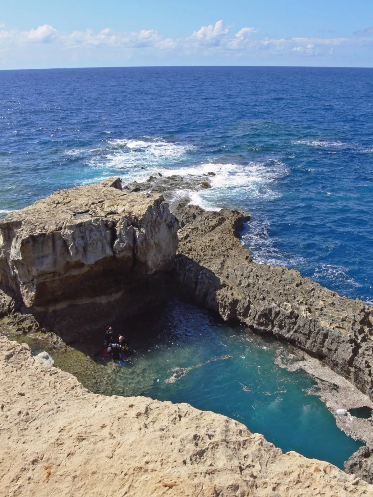The round Blue Hole pool cut into the limestone shore at Dwejra, Gozo, with open sea beyond