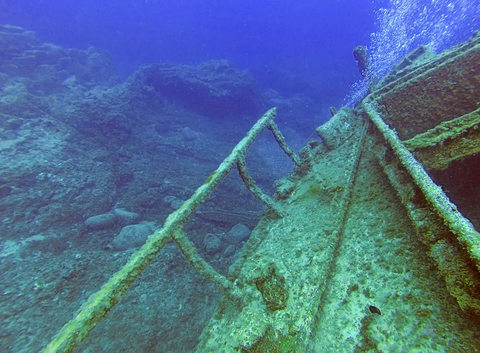 A diver hovers above the corroded metal frame of the El Condesito wreck in green water — Tenerife