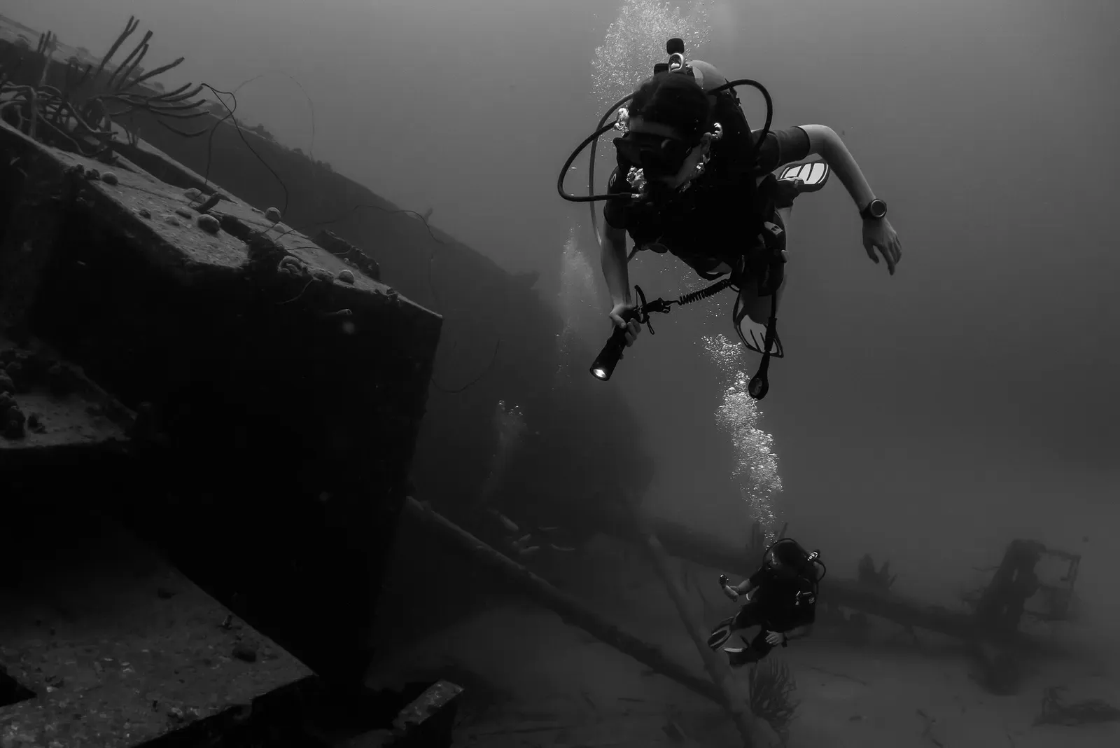 Two divers with torches exploring the sunken freighter Hilma Hooker in black and white — Bonaire