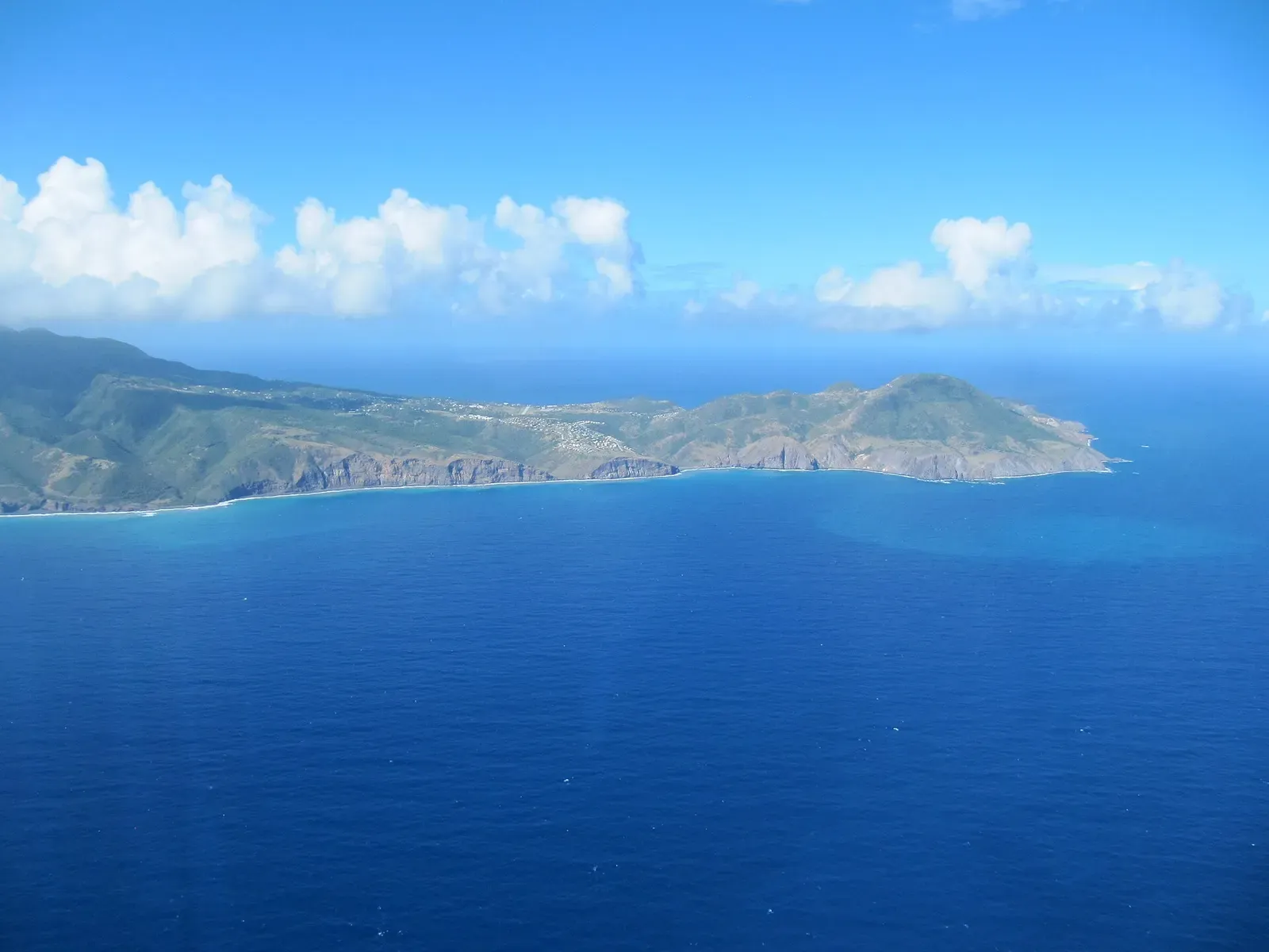 Aerial view of a green, hilly island ringed by deep blue sea under scattered white clouds — Montserrat