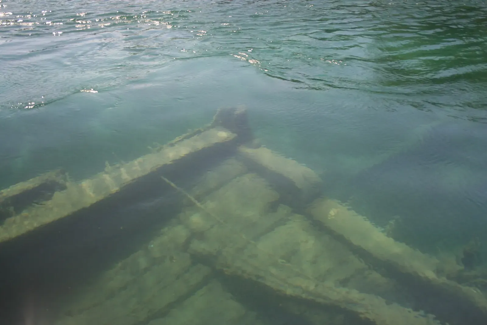 Wreck timbers and deck beams visible below the surface in greenish harbour water — Sweepstakes, Tobermory