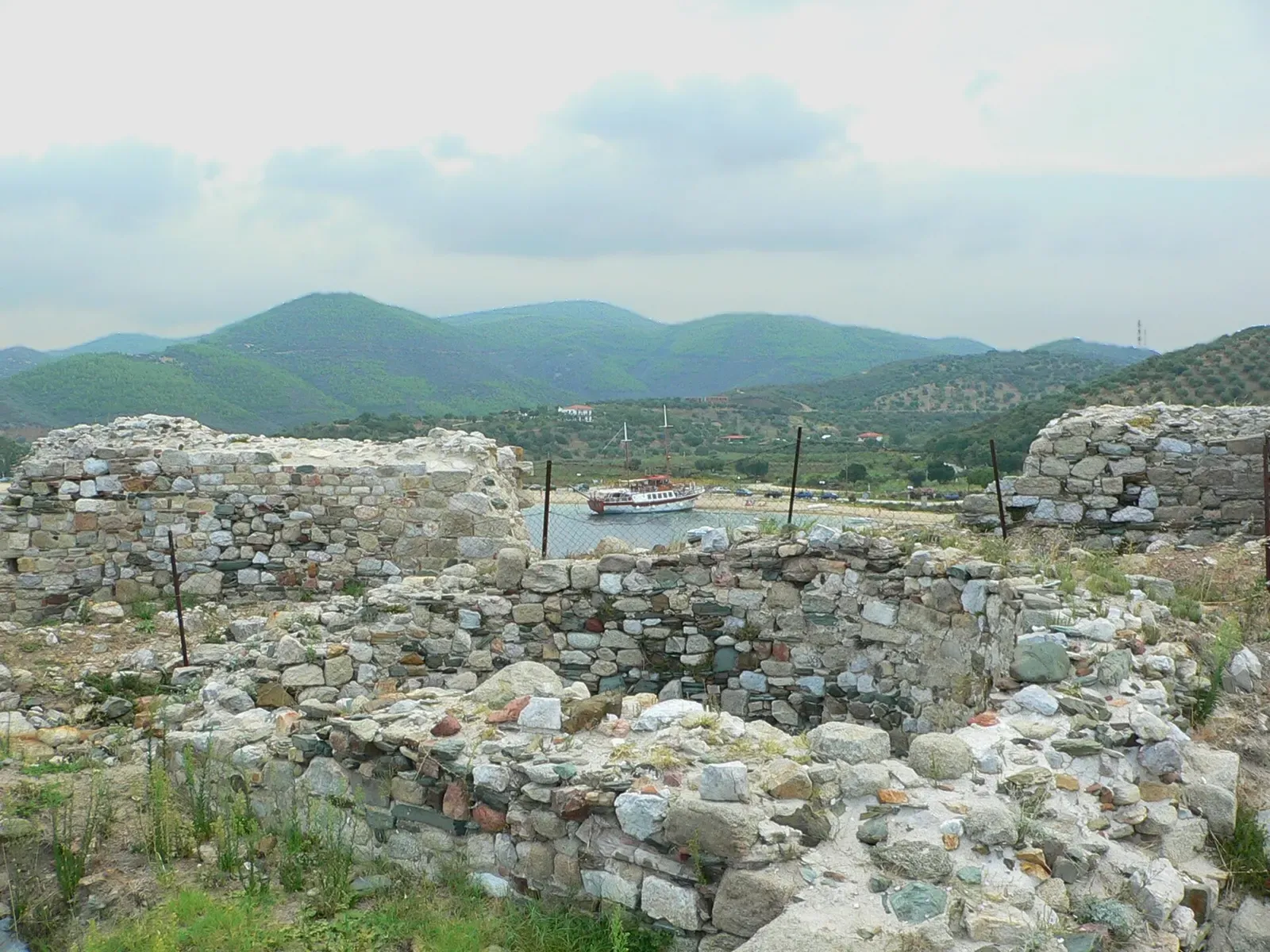 Ancient ruined walls overlooking Toroni harbour with a boat and green hills