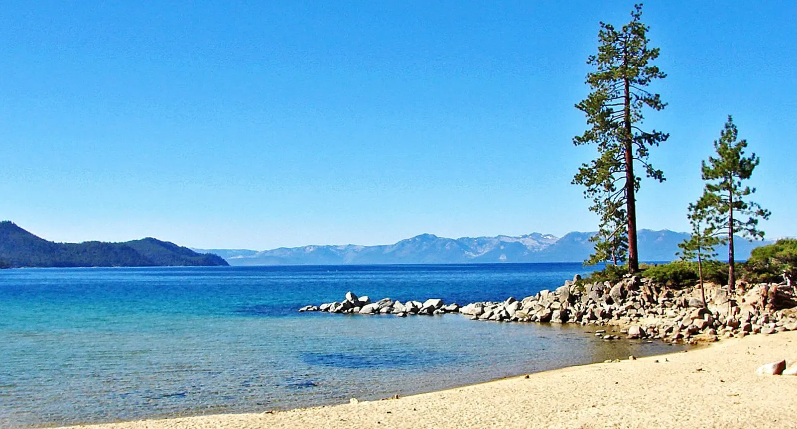 Granite boulders in shallow clear water at Sand Harbor with mountains beyond