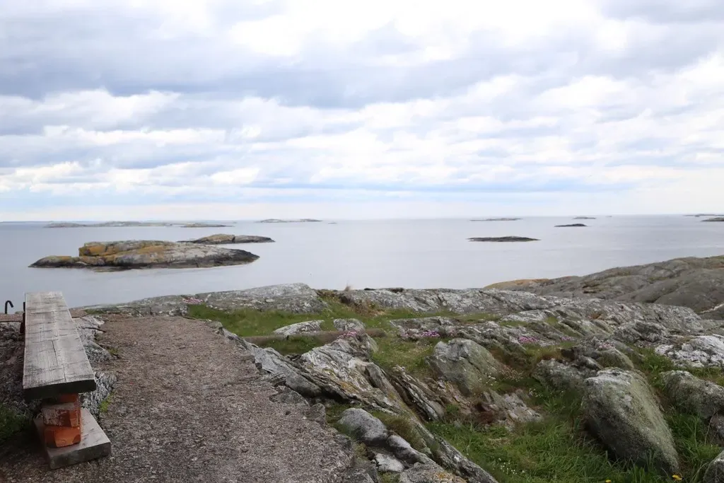 A gravel path and wooden bench on bare granite, looking out over calm grey sea dotted with low rocky skerries — Väderöarna