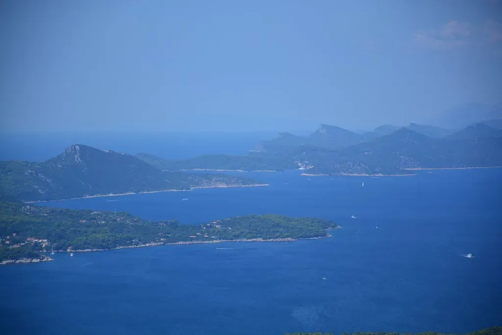 Wooded islands and narrow channels spread across a deep blue sea, with hazy mountains behind — Dubrovnik & the Elafiti Islands