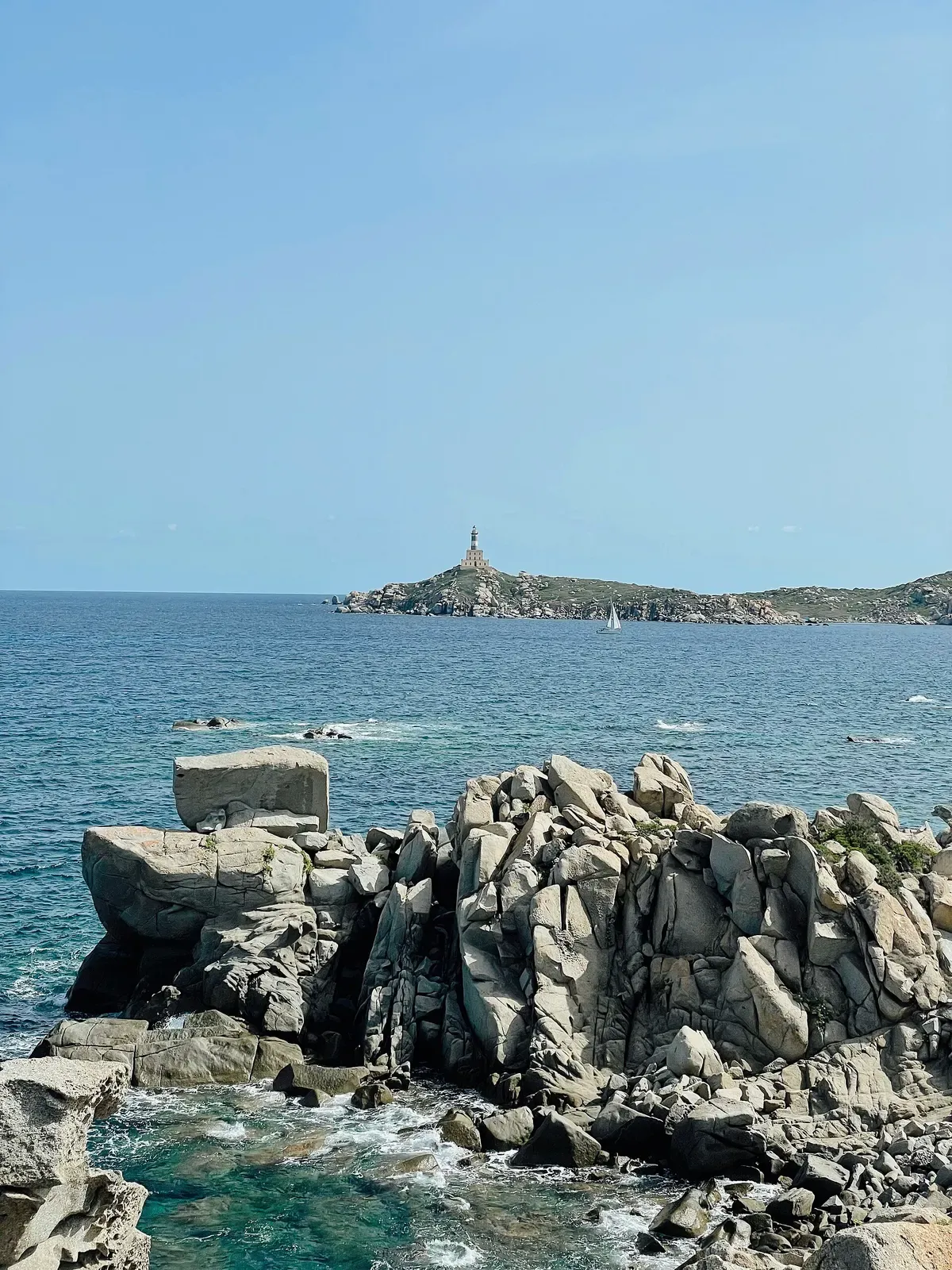 Granite rocks in the foreground with Isola dei Cavoli and its lighthouse across open water — Capo Carbonara