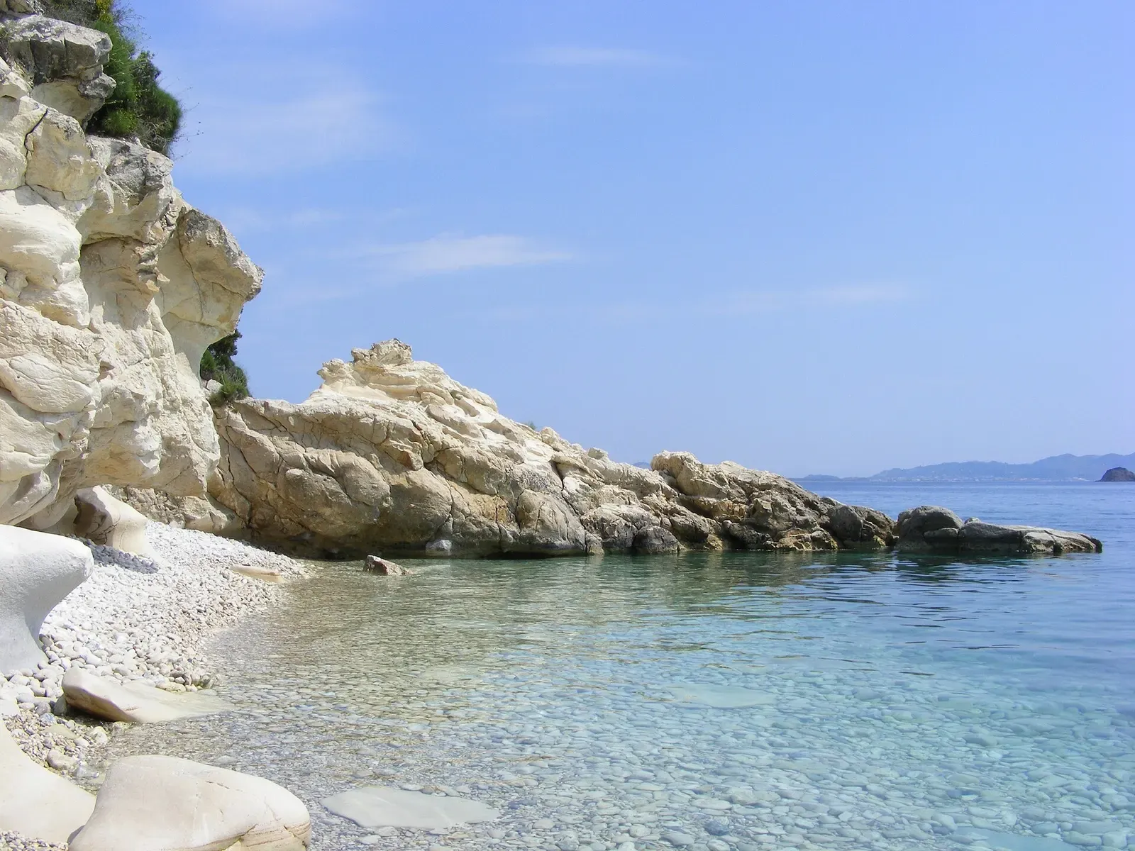 Clear turquoise water beside a jagged limestone rock at Marathias Beach, Zakynthos.
