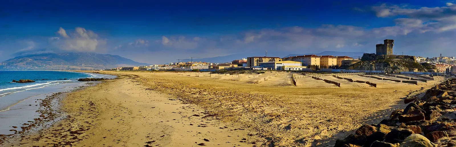 Wide golden-hour view of Tarifa town and its castle seen across the beach from Cape Punta Tarifa.