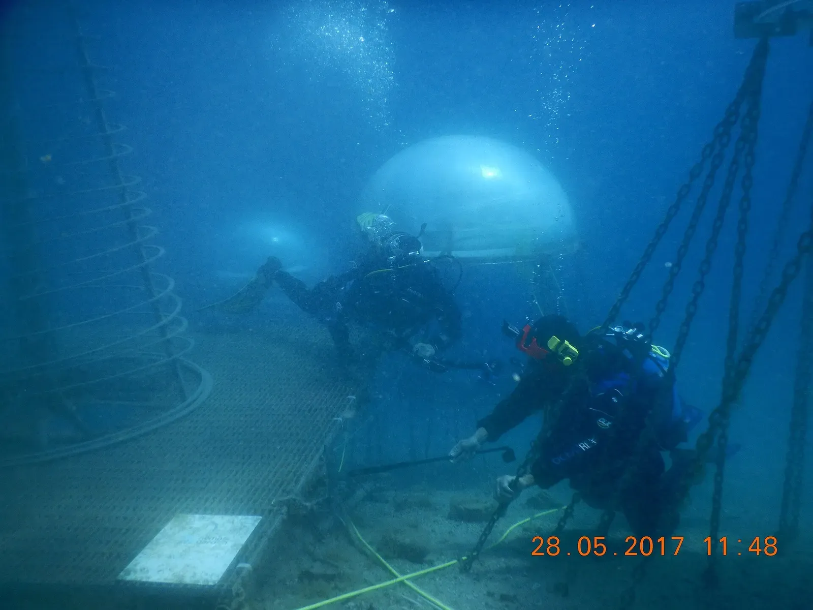 Two divers beside a chained-down biosphere dome on the seabed
