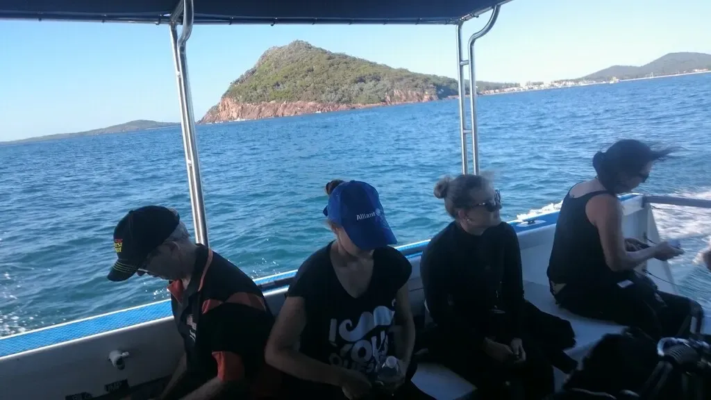 Divers seated on a dive boat with Broughton Island's cliffs ahead — Nelson Bay