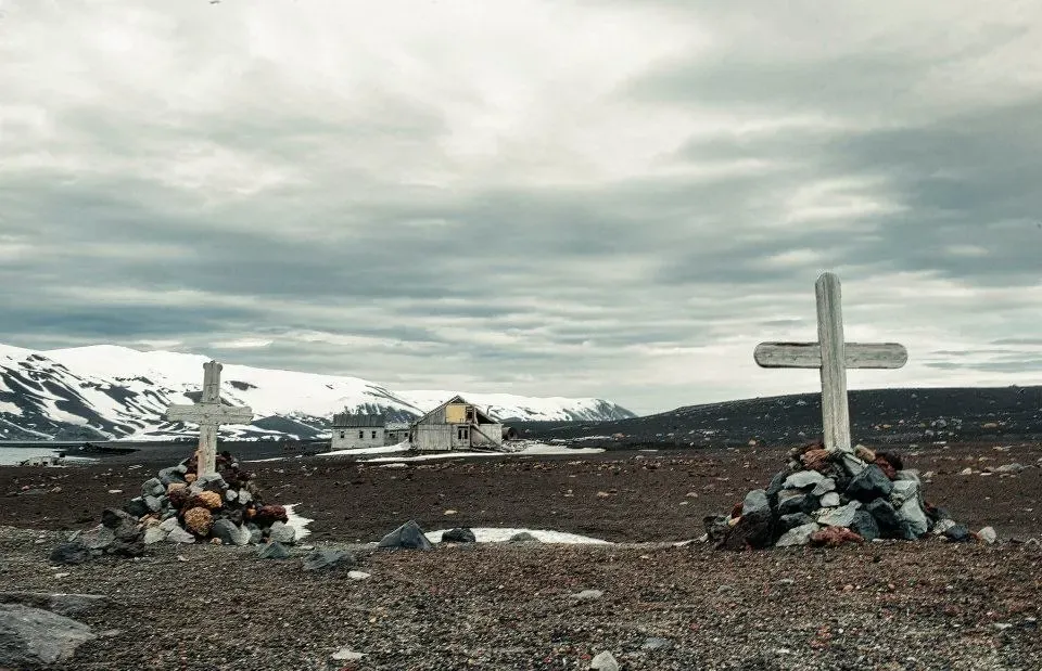 Ruined whaling station buildings and a memorial cross on the shore of Deception Island — Antarctic Peninsula