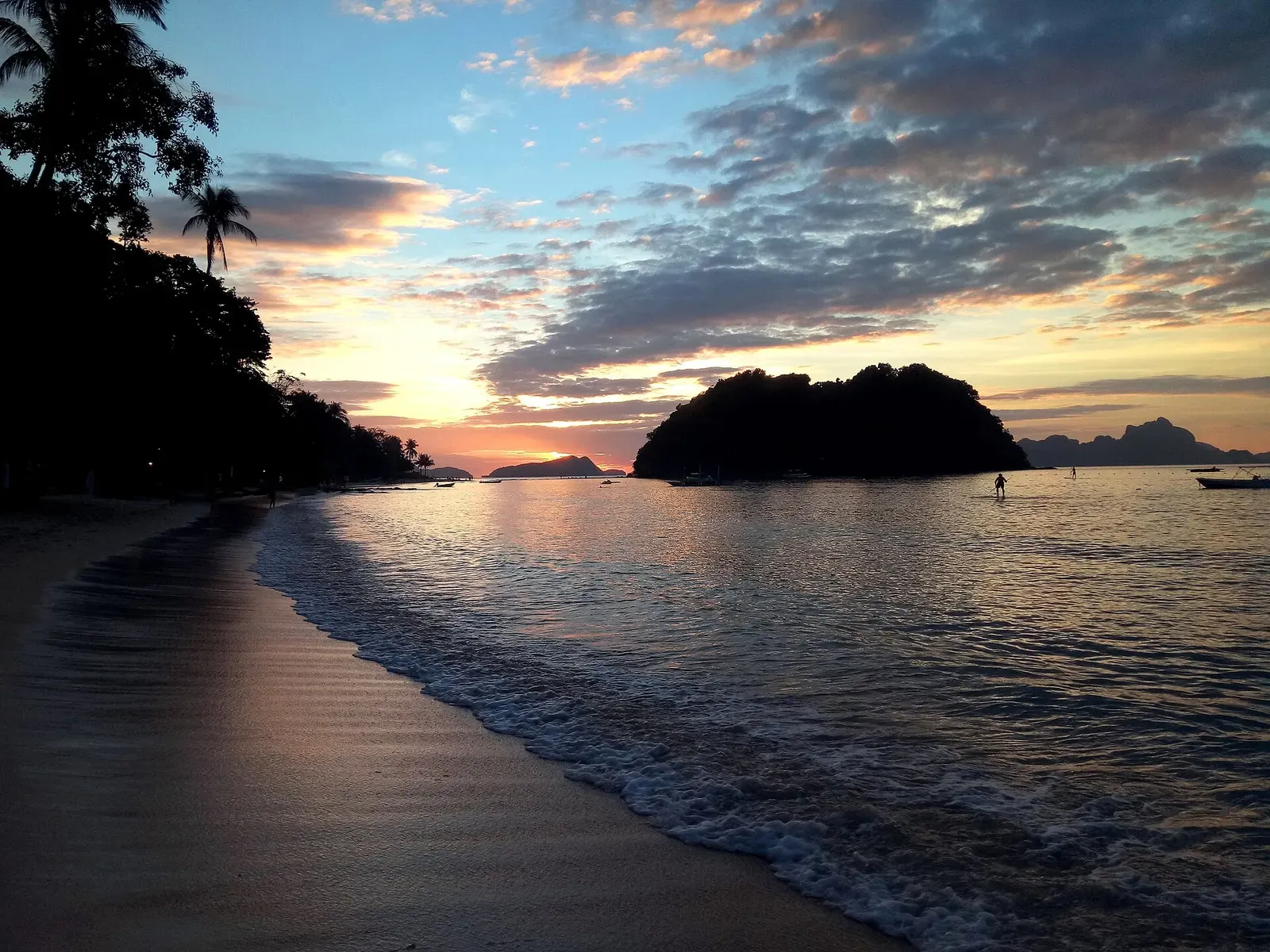 Sunset over a beach cove in El Nido with a small limestone island silhouetted offshore