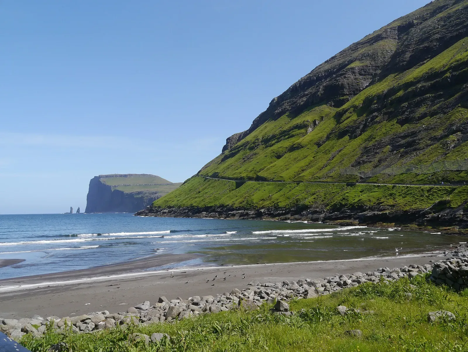 Steep green valley opening onto Tjørnuvík's beach and bay, seen from the approach road — Shores at Tjørnuvík, Faroe Islands