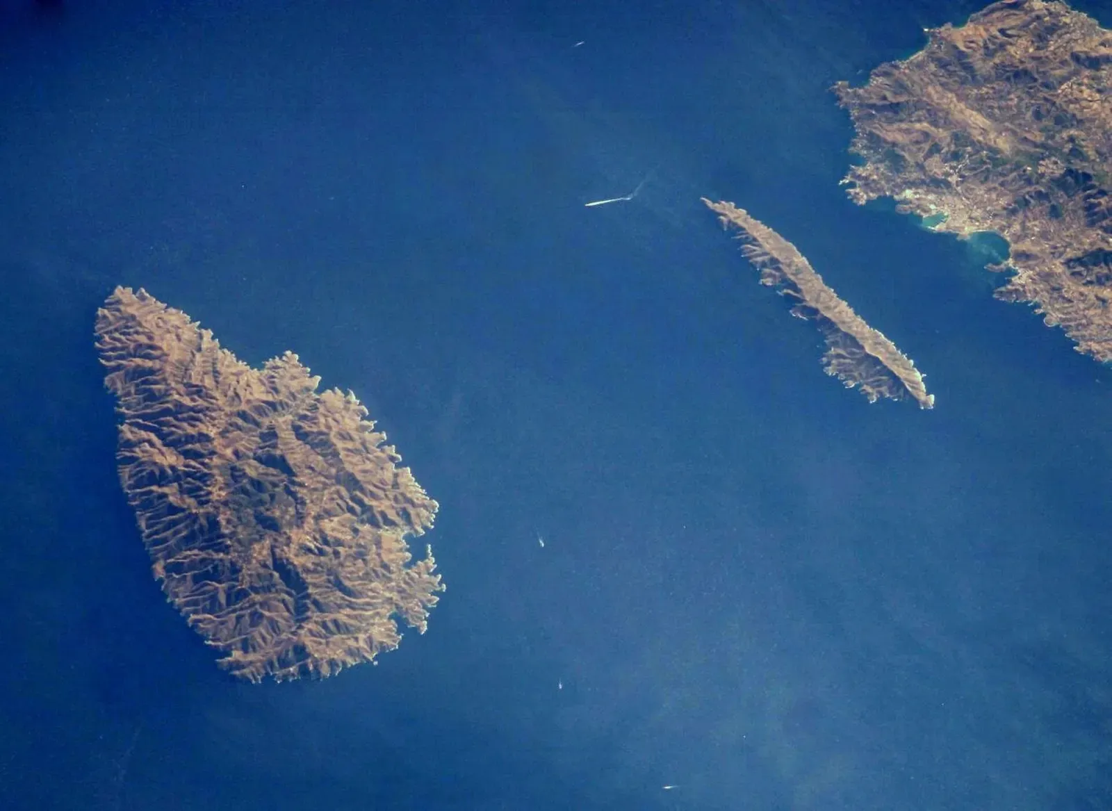 NASA astronaut photograph from orbit of the island of Kea, the narrow island of Makronisos, and Cape Sounion, with open blue water between them.