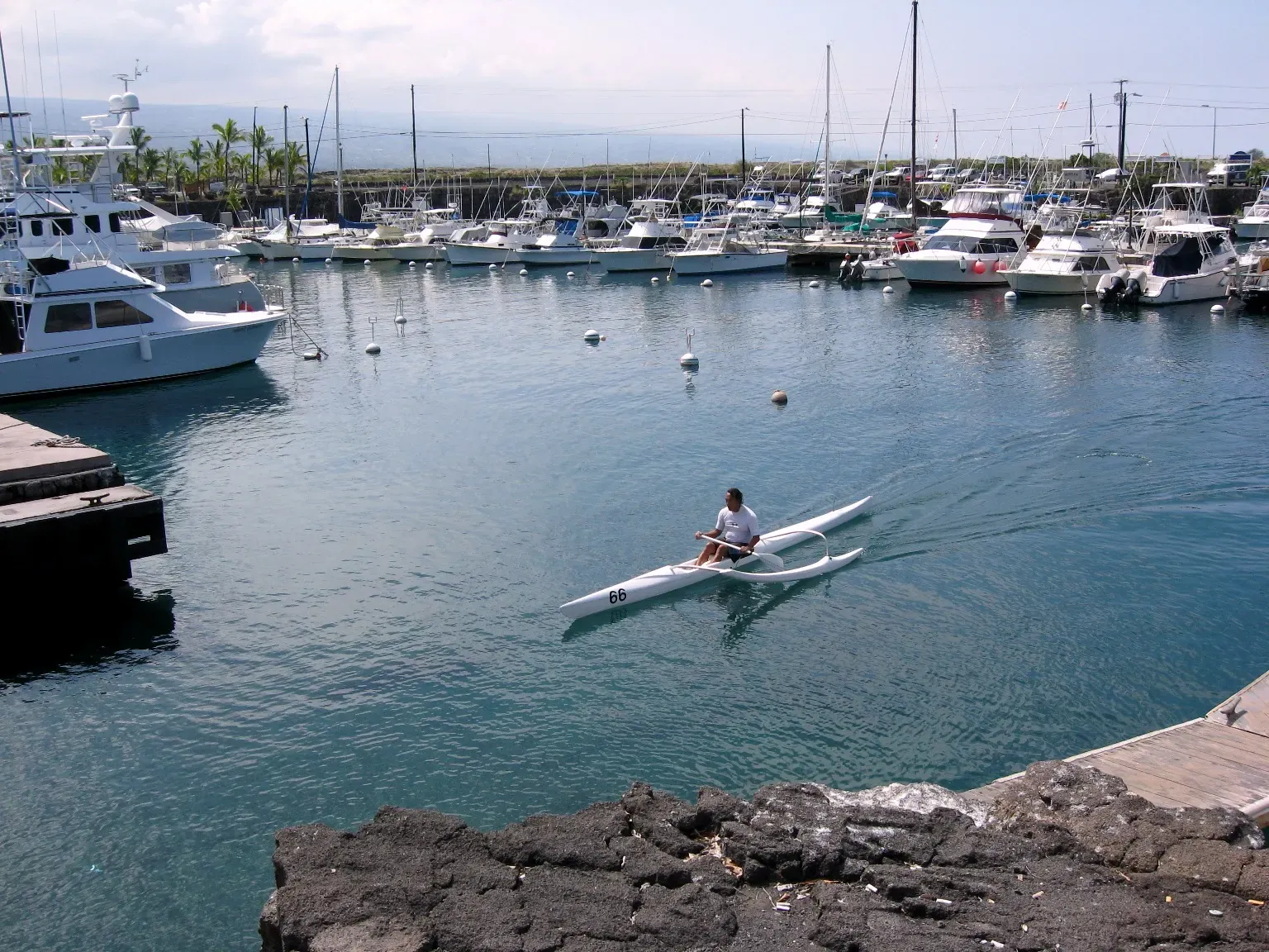 Fishing and charter boats moored inside Honokohau Harbor, with a lava breakwater and the slopes of the Big Island behind — Kona