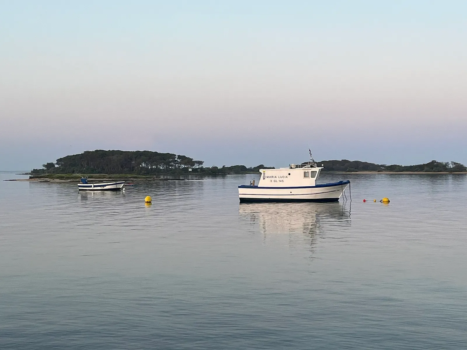 Two white and blue boats moored on calm water off a low wooded island at dawn, with yellow buoys — Porto Cesareo & the Nardò Coast