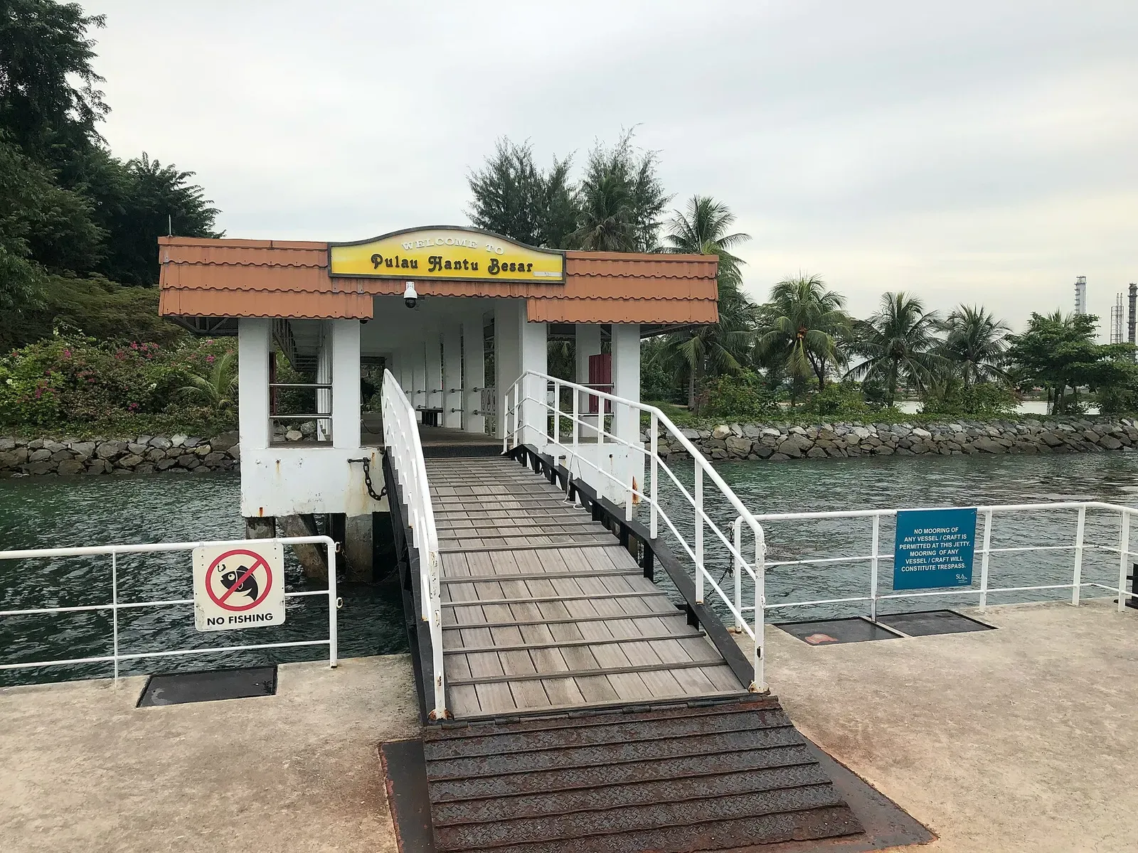 A white jetty building with a red tiled roof and a Pulau Hantu Besar sign, a gangway leading down to the landing