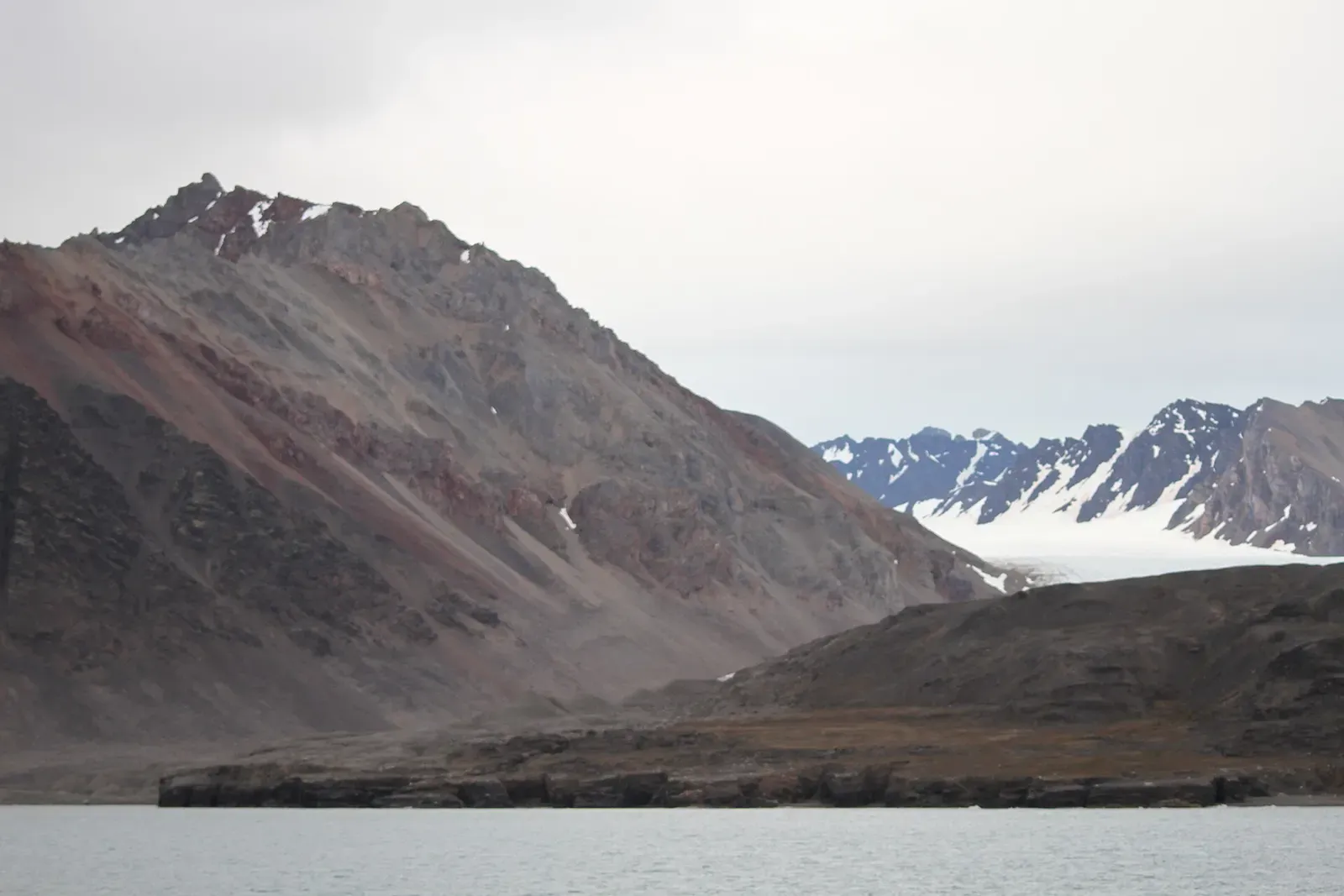 Bare mountain slopes rise above the shoreline of Blomstrandhamna in northern Kongsfjorden — Svalbard.