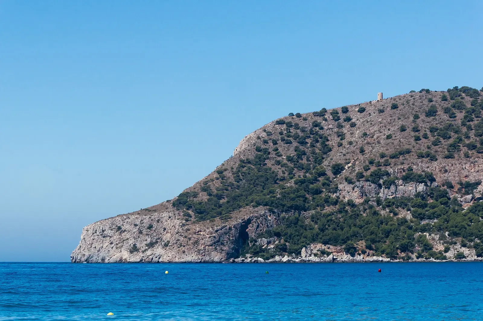 A rocky, tree-covered headland rises above the sea near La Herradura.