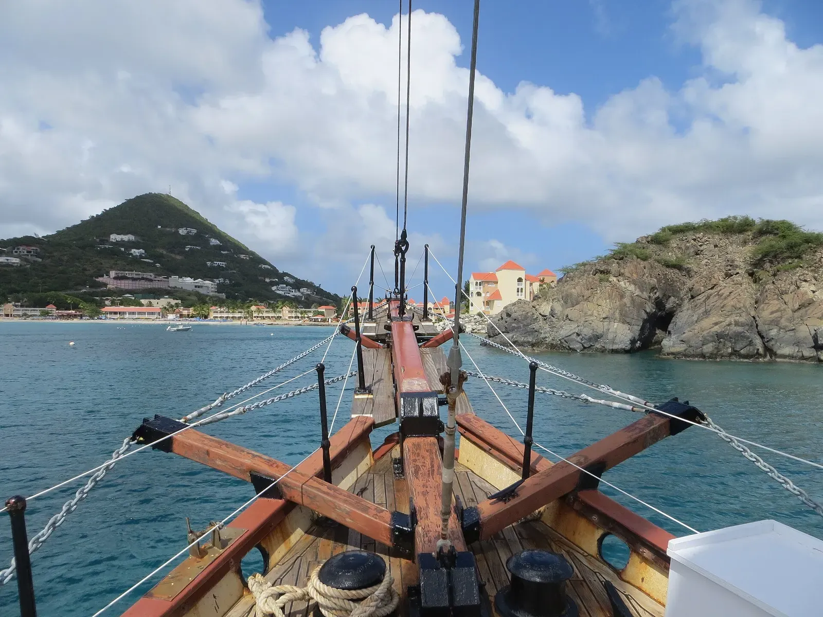 Tall ship's bowsprit and rigging framing the hills of Little Bay, Sint Maarten