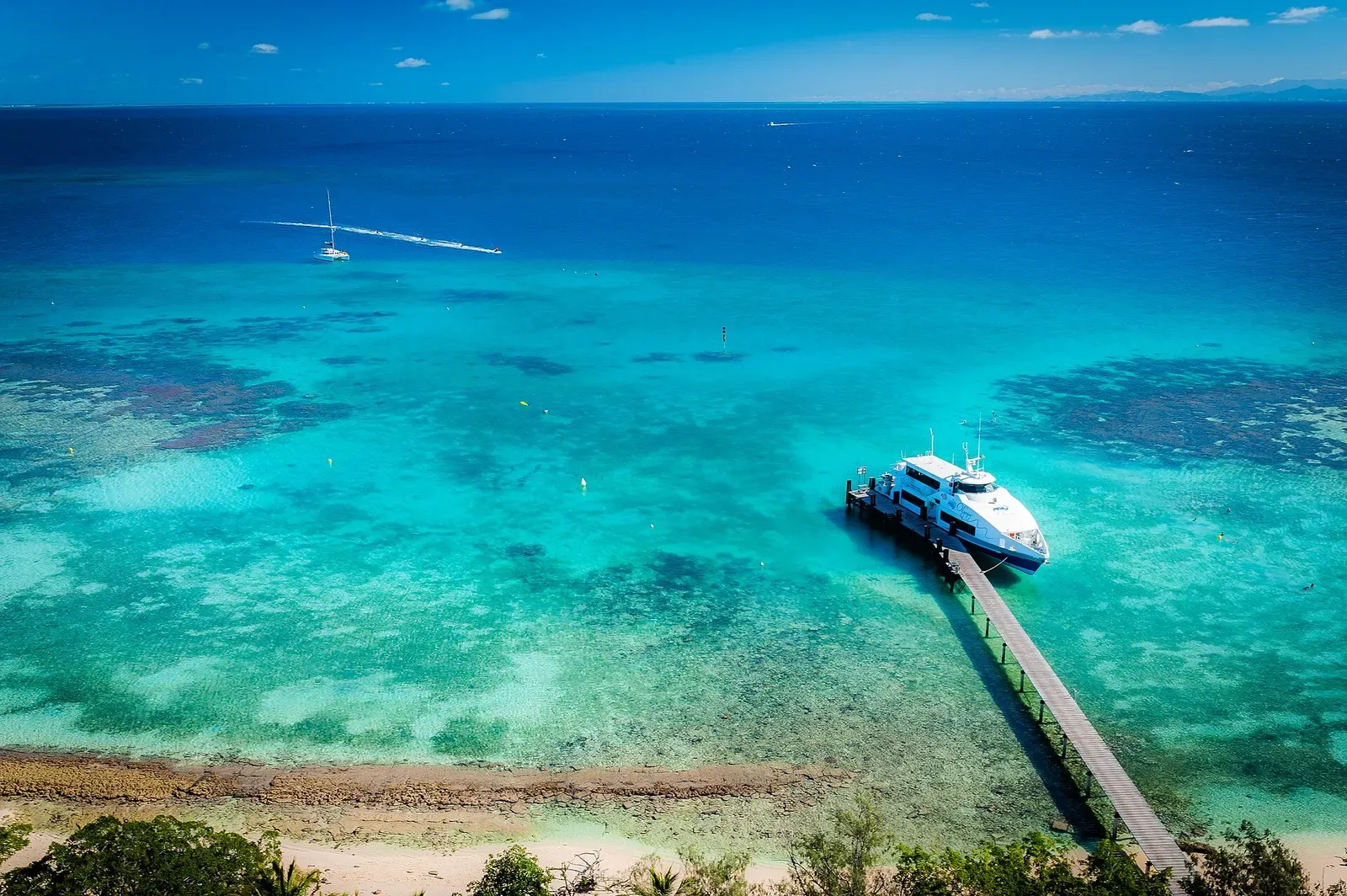 Aerial view of turquoise lagoon water and a dive boat moored at a jetty near Amédée islet — New Caledonia