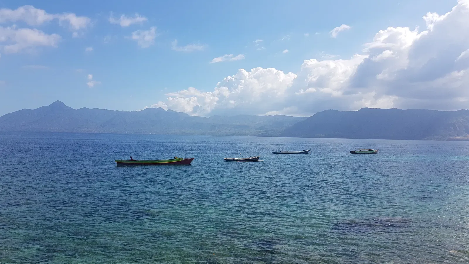 Small fishing boats anchored in calm blue water off Ternate Island with mountains beyond — Alor