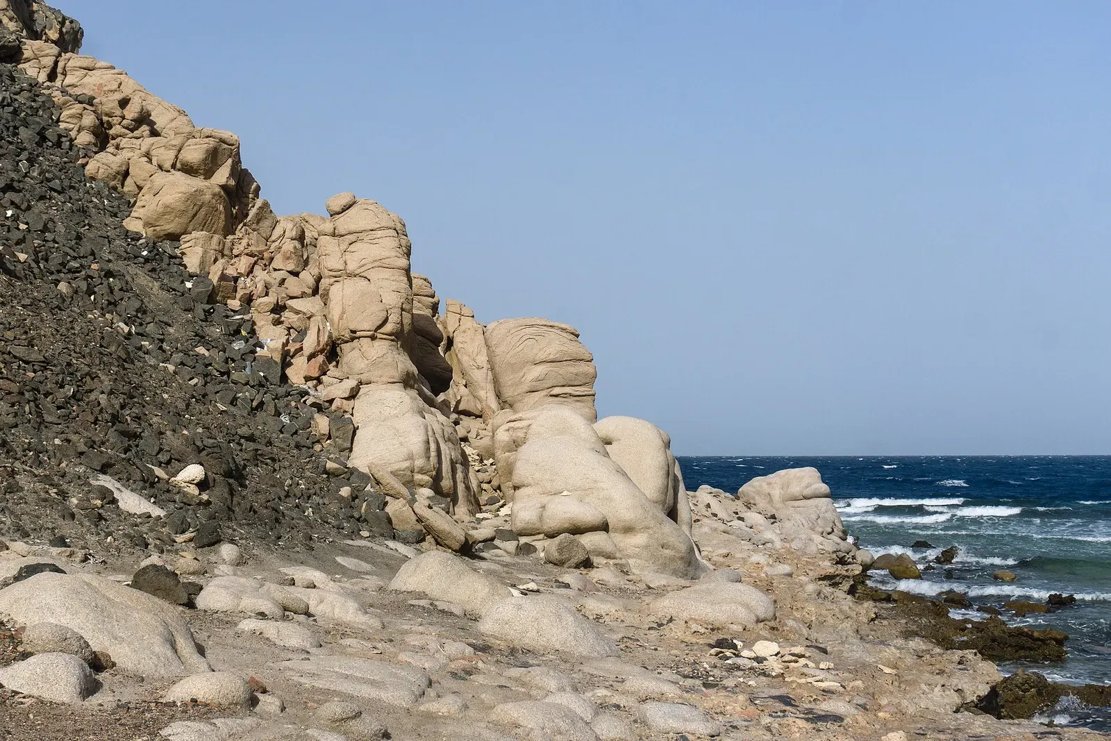 Weathered granite boulders piled at the shoreline with mountains behind — Ras Abu Galum, Dahab