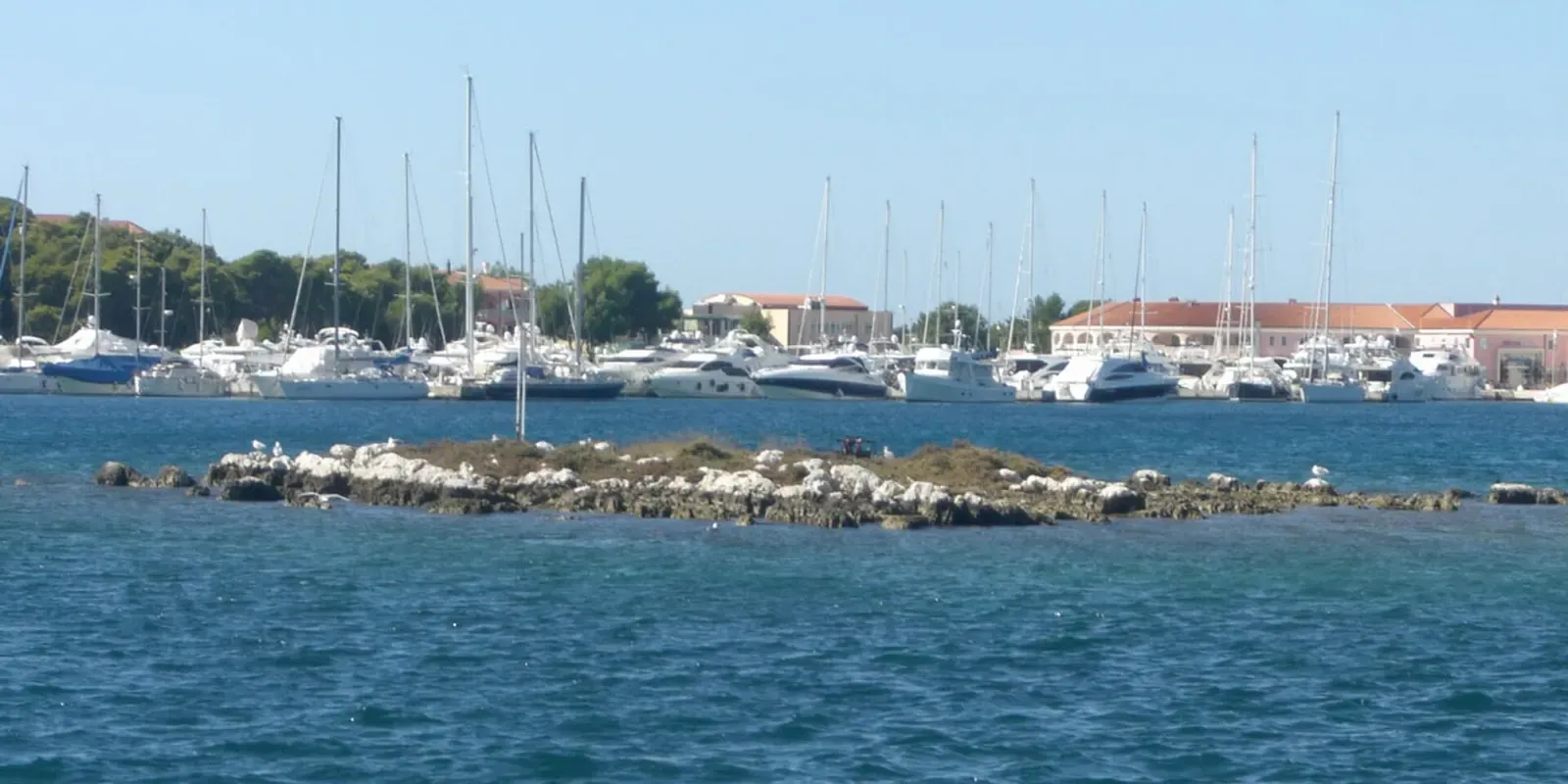 A small rocky islet beside moored yachts at Marina Frapa in Rogoznica.