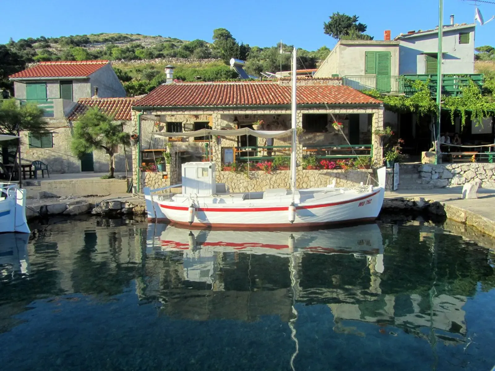 A traditional gaff-rigged boat moored in the small harbor below Smokvica Vela's stone houses — Smokvica Vela Wall, Kornati Islands.