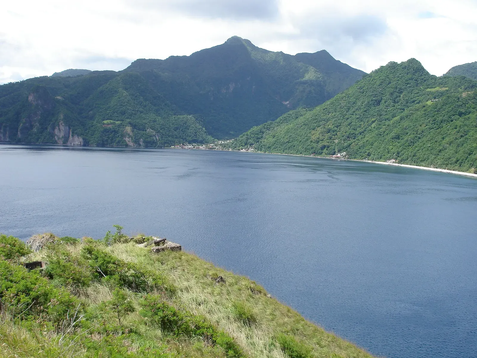 Evening light over Soufriere Bay's ridgeline seen from the grassy hillside above the water — L'Abym, Dominica