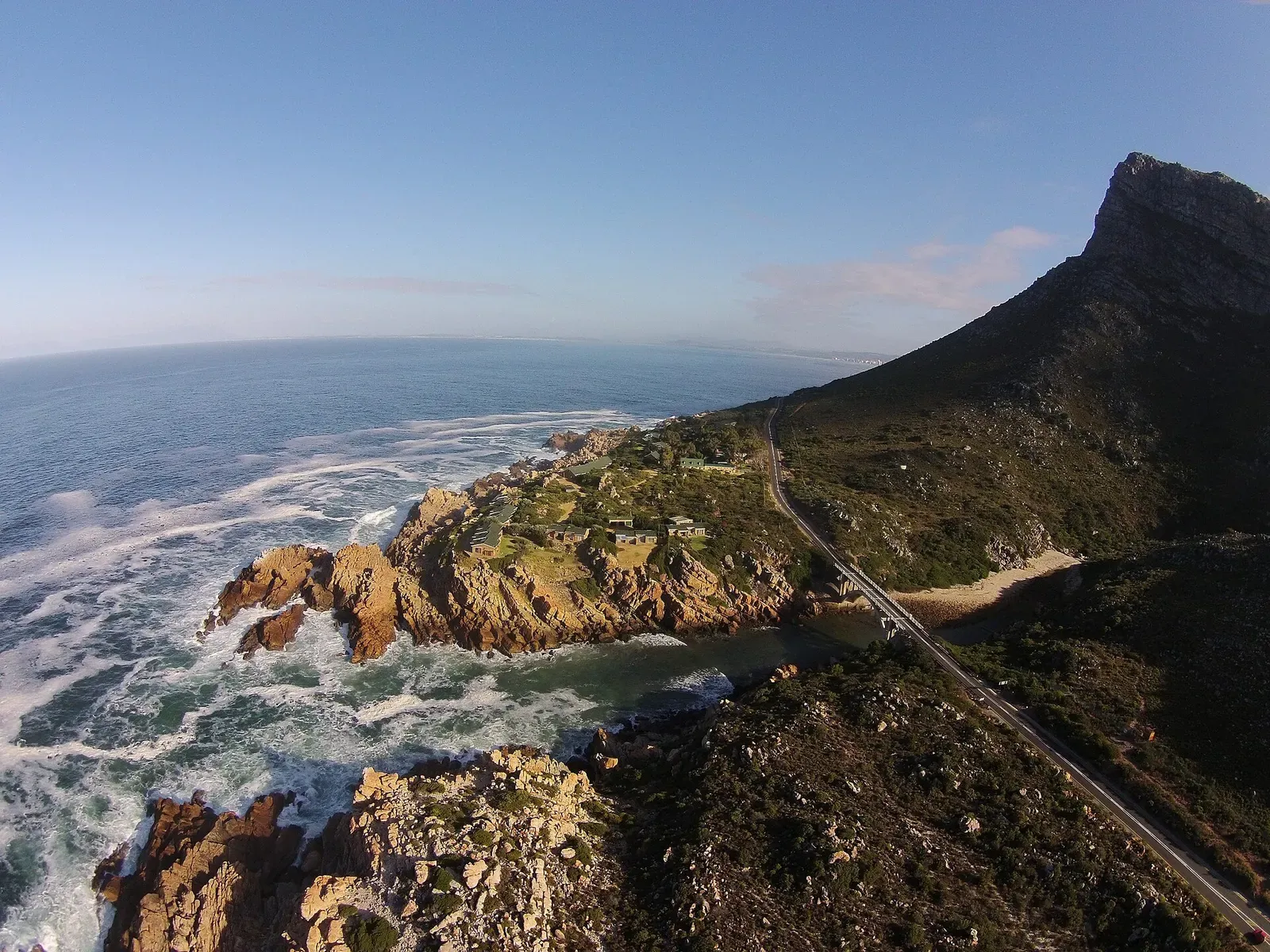 Aerial view of a rocky headland and river mouth with a coastal road running along the mountain slope — Rocky Bay, Gordon's Bay & Rooi-Els