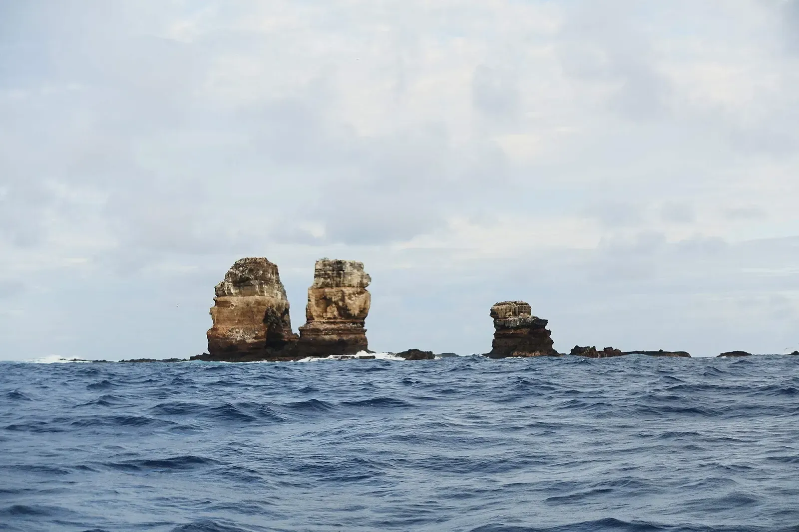 Two bare rock pillars standing in open ocean where the arch once stood — Darwin's Arch, Galápagos.