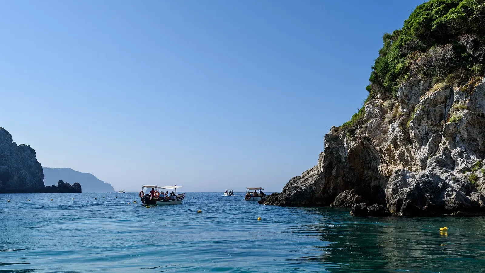 Swimmers in a turquoise cove beneath pale cliffs at the Paleokastritsa sea caves, Corfu.