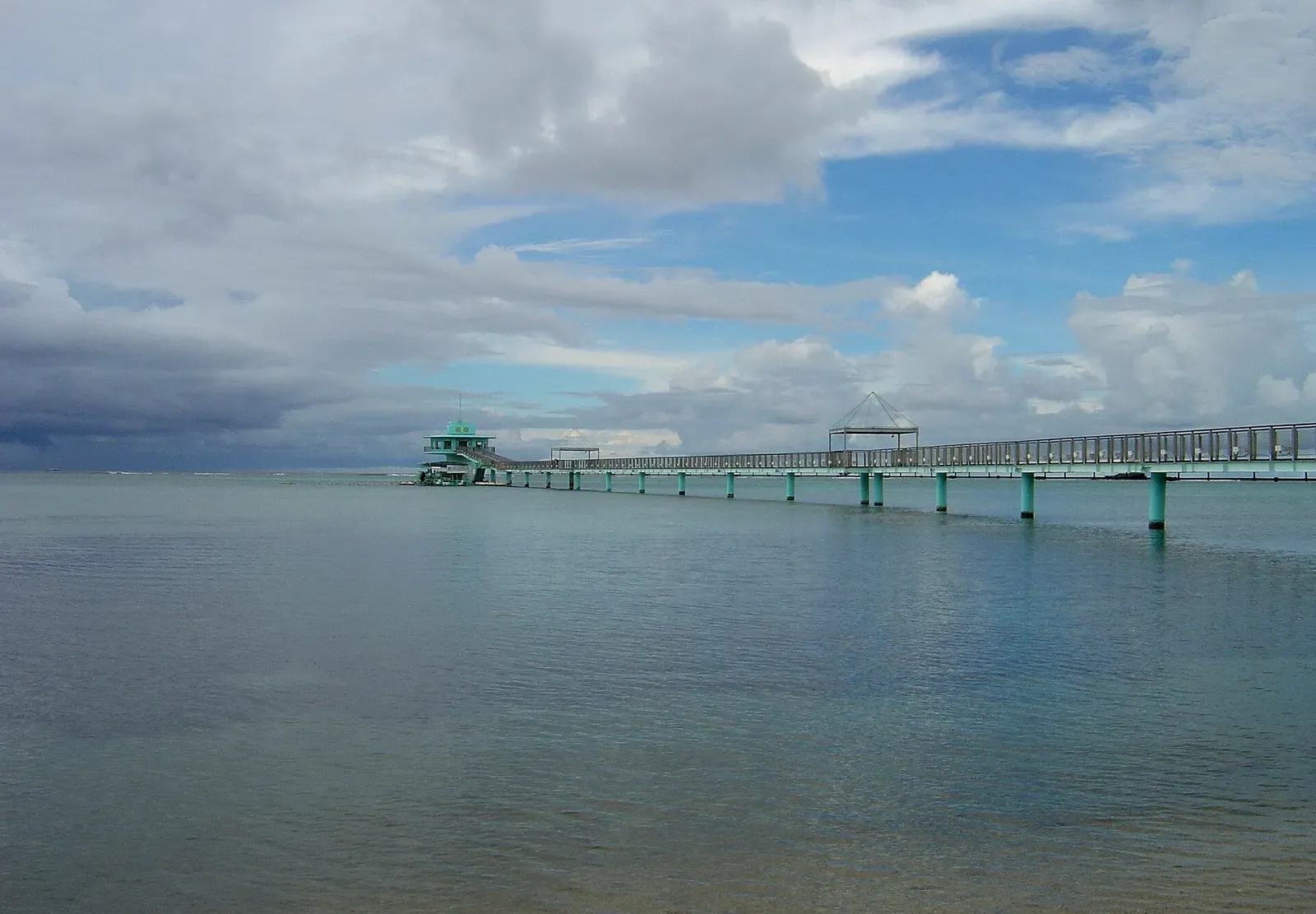 A pier stretches across calm lagoon water to a distant elevated tower — Piti Bomb Holes, Guam